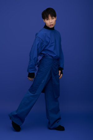 A bright blue backdrop highlights a young, handsome Asian man in modern fashion.のeditorial素材