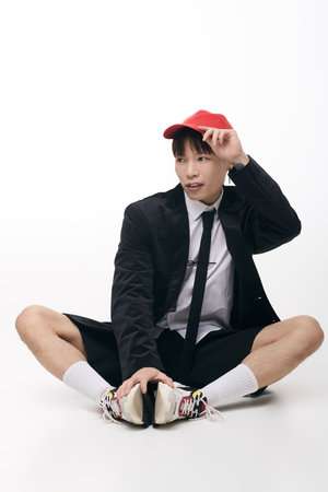 Charming young man showcases modern fashion with confidence, sitting comfortably in a studio.のeditorial素材