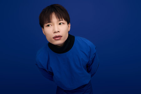 A striking young asian man displays his charm while standing against a bold blue background.の写真素材