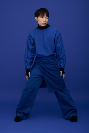 Handsome young Asian man poses confidently in an artistic blue outfit against a rich backdrop.のeditorial素材
