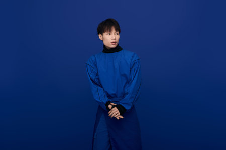 A stylish young Asian man confidently poses in a chic blue outfit, exuding charisma.の写真素材