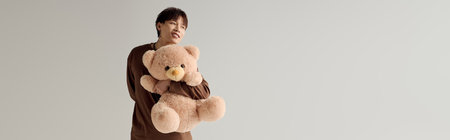 A lively young asian man radiates joy holding a soft teddy bear in a well lit indoor space.の写真素材