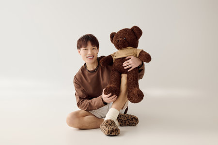 A young man sits on the floor, joyfully hugging a teddy bear, radiating warmth.の写真素材