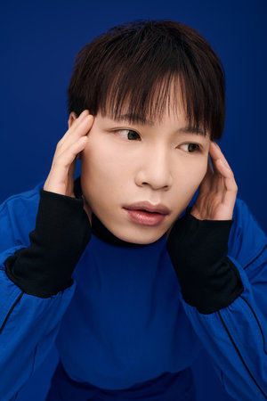 A young Asian man reflects deeply in a vivid blue, emotional surroundings.の写真素材