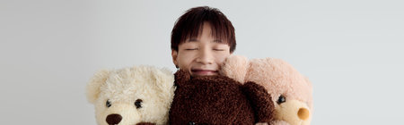 A young handsome Asian man smiles brightly while hugging three adorable teddy bears in a cozy room.の写真素材