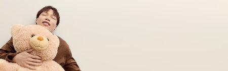 Cheerful young man enjoys a moment of comfort while hugging a large teddy bear with a warm smile.の写真素材