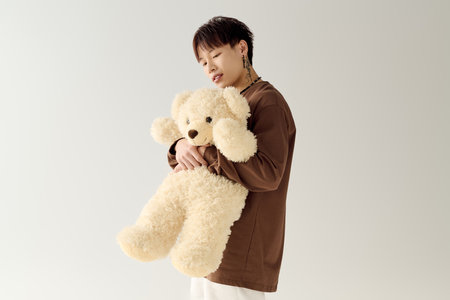 A charming young man cradles an oversized teddy bear, showcasing a playful and heartwarming vibe.の写真素材