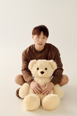 A charming young man shares a moment with a fluffy teddy bear indoors.の写真素材