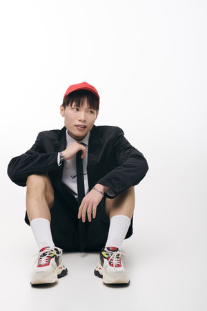 Confident young man dressed in a suit and cap sits playfully on the floor, showcasing his style.の写真素材