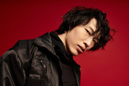 Asian man in black jacket looks down against red.の写真素材