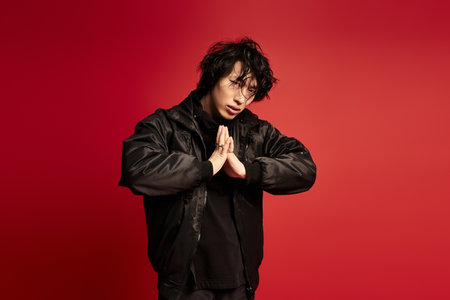 A stylish young man in black attire posing in a red studio.