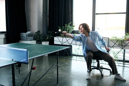 A young, attractive man takes a shot at table tennis while enjoying downtime in his office.の写真素材