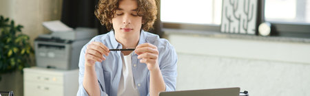 Young man with curly hair thinks with a pen in a modern, bright office.