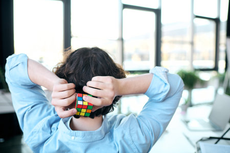 A young man with striking features takes a moment to unwind, solving a Rubiks cube at work.