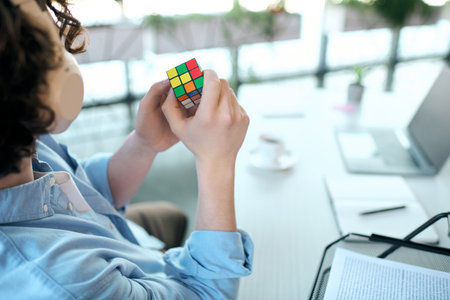 A good looking young man focuses on solving a colorful puzzle while sitting at his office desk.の写真素材