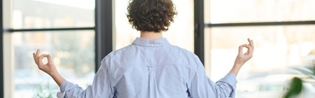 Handsome young man with curly hair engages in mindful meditation at work during a quiet moment.の写真素材