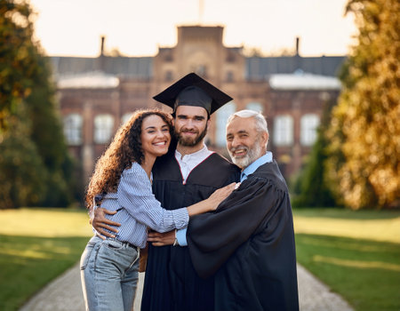 Joyful family embraces a graduate in university attire surrounded by stunning green scenery.の素材