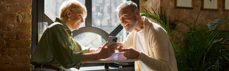 A middle-aged couple smiles and shares a moment while looking at their phone at a cafe.
