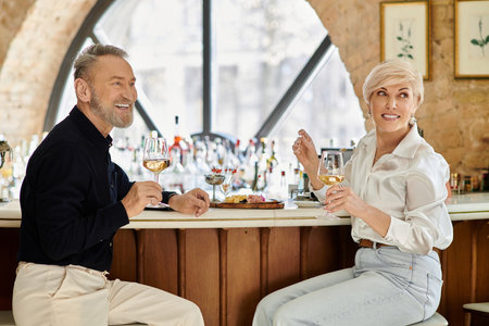 A delightful evening unfolds as a middle aged couple enjoys wine and conversation at a stylish bar.の写真素材