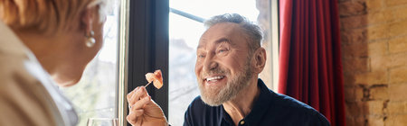 A mature couple shares laughter and smiles over dinner in a cozy restaurant setting, bannerの写真素材