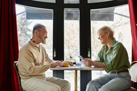 A middle aged man and woman share joyful conversation over warm drinks in a quaint setting.の写真素材