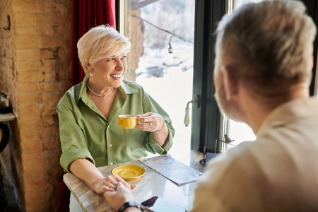 A middle aged couple smiles at each other while sipping tea in a quaint cafe on a sunny day.の写真素材
