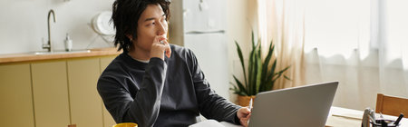 A handsome young asian student concentrates on his laptop while studying at home, bannerの写真素材