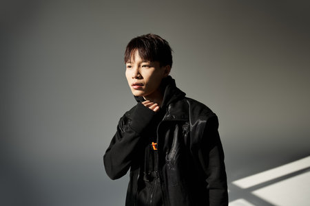 Confident Asian man with a relaxed vibe showcases modern style in bright light.の写真素材