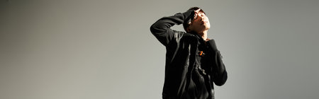 A fashionable young asian man expresses confidence while striking a pose in a studio setting.