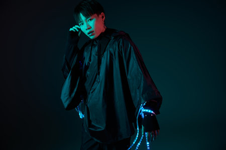 Confident young man poses in a striking outfit with bright details against a dark background.の写真素材