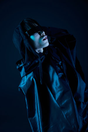 Handsome man in a stylish outfit poses dramatically under dim blue light, radiating confidence.の写真素材