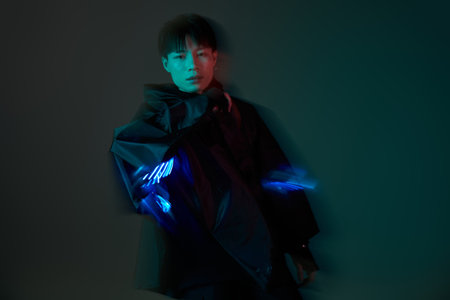 A handsome young Asian man poses confidently, displaying glowing hand effects in a dark setting.の写真素材