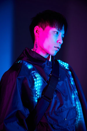 Handsome young individual showcases a fashionable attire illuminated with striking colors at night.の写真素材
