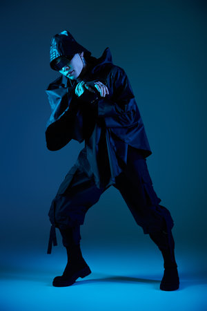 Handsome asian man strikes a dynamic pose in an eye catching outfit under vibrant blue lighting.の写真素材