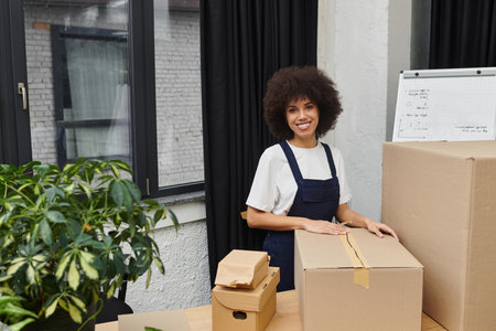 A young woman smiles while packing boxes in her stylish apartment.のeditorial素材