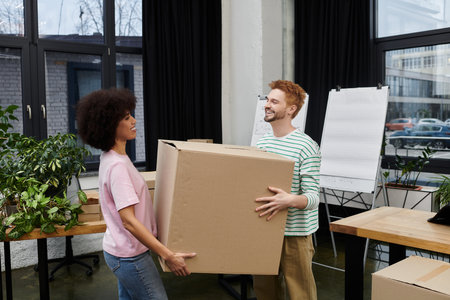 Two people joyfully pack and unpack boxes in a bright room filled with plants and moving supplies