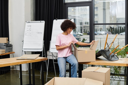 A young woman organizes items in a box at a stylish workplace with large windows.のeditorial素材