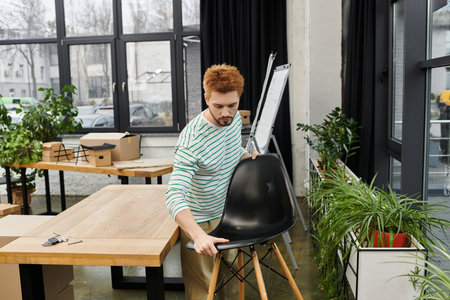 man carefully handles a black chair while unpacking in a contemporary office setting.の写真素材