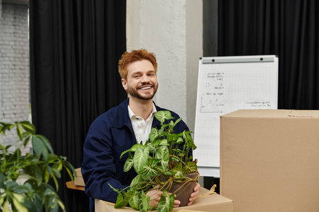 A man happily carries a potted plant among moving boxes in a modern setting.
