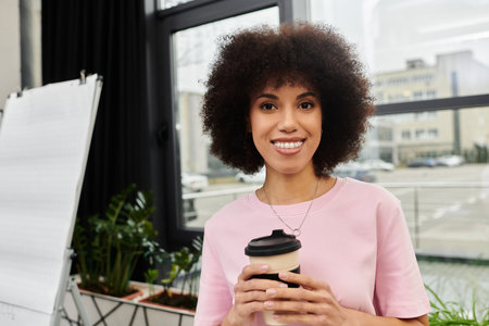 Young woman smiles while holding a coffee cup amidst a bustling move in process at work.の写真素材