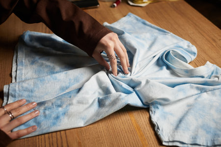 Young craftswoman skillfully designs a tie dye pattern on a light blue shirt in her workspace.の写真素材