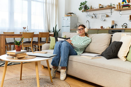 A young woman sits on a sofa, deep in thought as she writes in her stylish living room.のeditorial素材