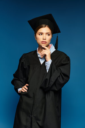 Confident woman in graduation gown and cap reflects on her aspirations in a modern setting.のeditorial素材