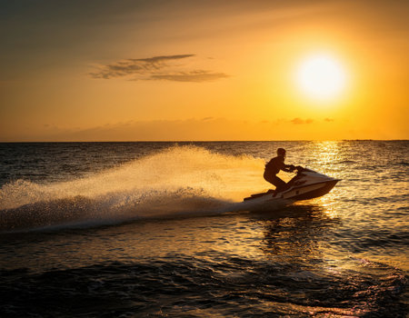 A person rides a jet ski on the shimmering sea at sunset, enhancing the adventurous vibe.の素材