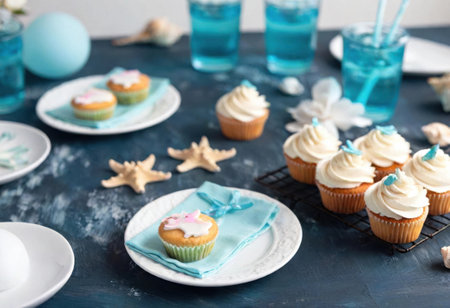 A vibrant table awaits with colorful cupcakes and refreshing blue drinks for the festive gathering.の素材