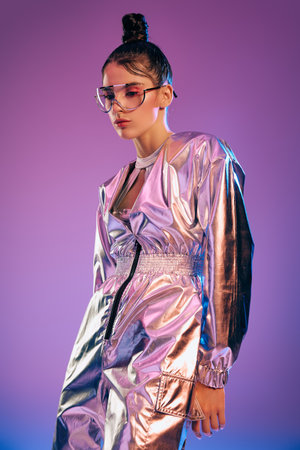 A stylish woman confidently poses in metallic attire with holographic colors in a creative setting.のeditorial素材