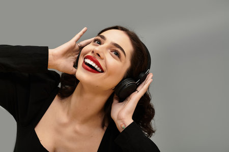 Young woman with braces and striking red lips smiles joyfully against a grey background.