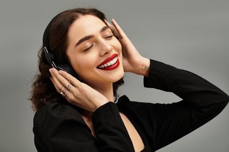A beautiful young woman with braces smiles joyfully while listening to music in a grey setting.