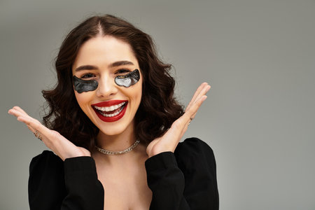 A radiant young woman showcases her braces and bright red lips, exuding charm on a grey background.のeditorial素材