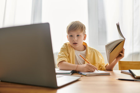 A little cute boy in comfy casual attire engages with his laptop while studying at home.の写真素材